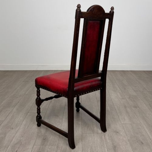 fig 3. A set of six dark oak dining chairs featuring red leather upholstery, carved crests, turned legs, and brass stud trimming.