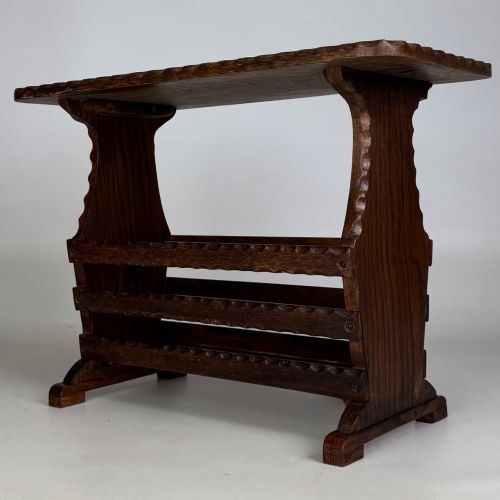 fig 1. A dark brown oak side table featuring a rectangular top with scalloped carved edges over an integrated three-slat magazine rack below.