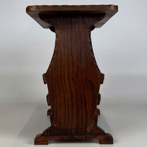 fig 2. A dark brown oak side table featuring a rectangular top with scalloped carved edges over an integrated three-slat magazine rack below.