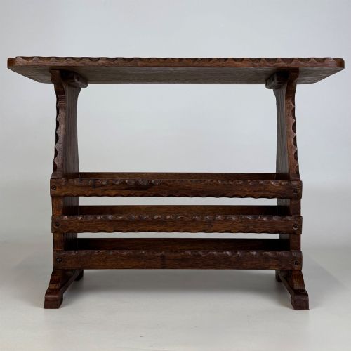 fig 4. A dark brown oak side table featuring a rectangular top with scalloped carved edges over an integrated three-slat magazine rack below.