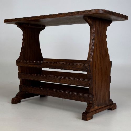 fig 5. A dark brown oak side table featuring a rectangular top with scalloped carved edges over an integrated three-slat magazine rack below.