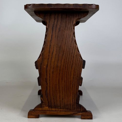 fig 6. A dark brown oak side table featuring a rectangular top with scalloped carved edges over an integrated three-slat magazine rack below.