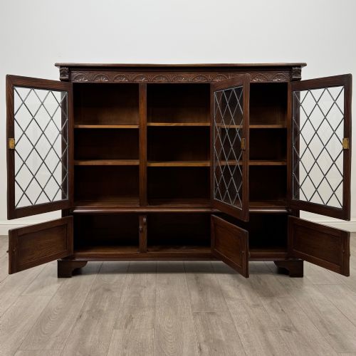 fig 1. A large dark brown carved oak display cabinet featuring three leaded glass doors over three carved cupboard doors with metal ring pulls.