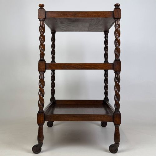 fig 2. A three-tier dark oak tea trolley featuring spiralled barley twist corner supports, turned top finials, and castor wheels.