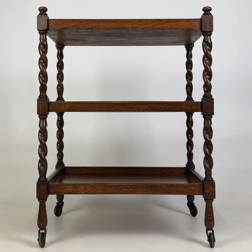 fig 4. A three-tier dark oak tea trolley featuring spiralled barley twist corner supports, turned top finials, and castor wheels.