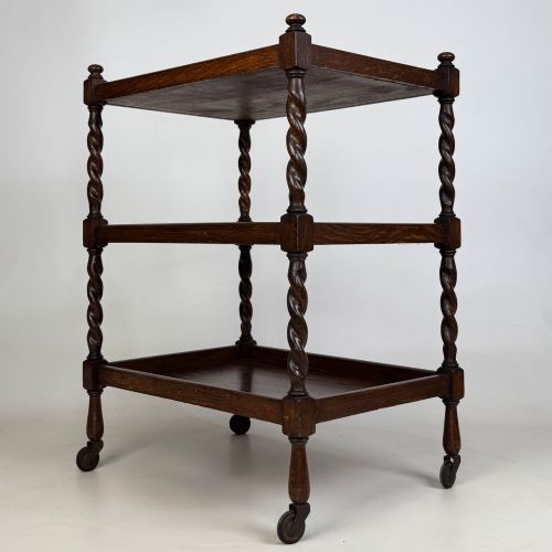 fig 5. A three-tier dark oak tea trolley featuring spiralled barley twist corner supports, turned top finials, and castor wheels.