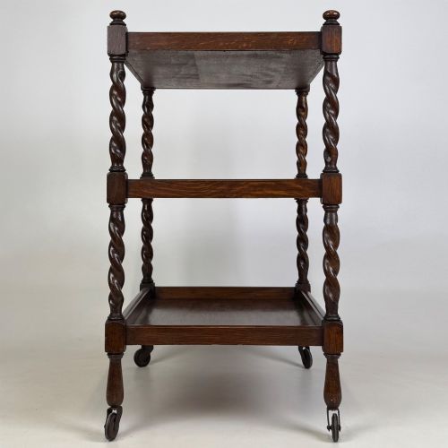 fig 6. A three-tier dark oak tea trolley featuring spiralled barley twist corner supports, turned top finials, and castor wheels.