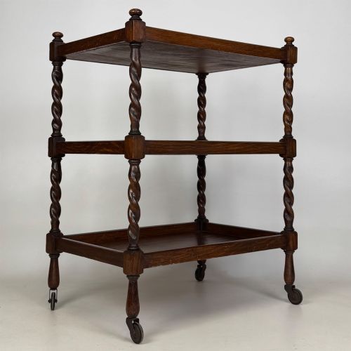 fig 7. A three-tier dark oak tea trolley featuring spiralled barley twist corner supports, turned top finials, and castor wheels.