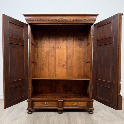 fig 1. A 19th-century French walnut wardrobe with double doors featuring detailed carved foliate panels, central fluted columns, two lower drawers, and a stepped cornice.