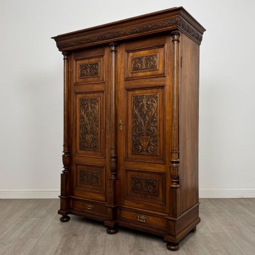 fig 2. A 19th-century French walnut wardrobe with double doors featuring detailed carved foliate panels, central fluted columns, two lower drawers, and a stepped cornice.