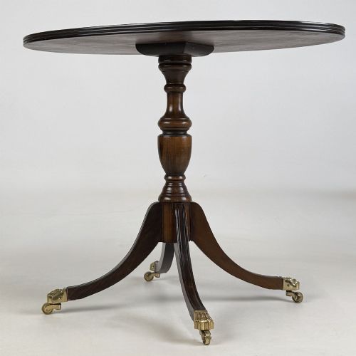 fig 1. A dark brown oak pedestal side table with an oval top, turned central column, and swept legs featuring brass paw castors.
