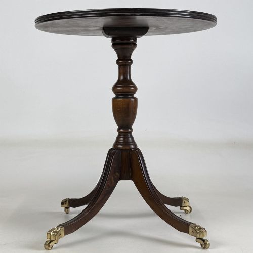 fig 2. A dark brown oak pedestal side table with an oval top, turned central column, and swept legs featuring brass paw castors.