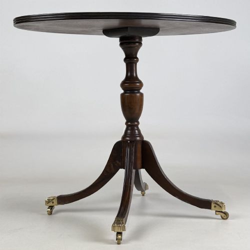 fig 3. A dark brown oak pedestal side table with an oval top, turned central column, and swept legs featuring brass paw castors.
