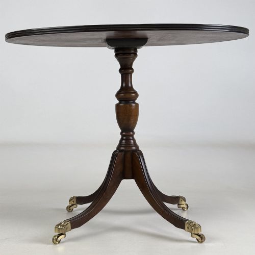fig 4. A dark brown oak pedestal side table with an oval top, turned central column, and swept legs featuring brass paw castors.