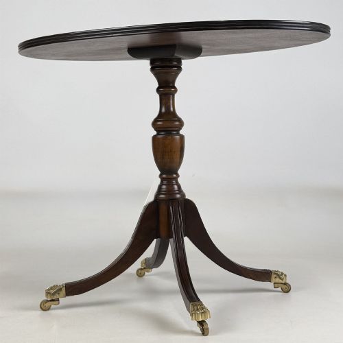 fig 5. A dark brown oak pedestal side table with an oval top, turned central column, and swept legs featuring brass paw castors.