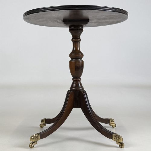 fig 6. A dark brown oak pedestal side table with an oval top, turned central column, and swept legs featuring brass paw castors.