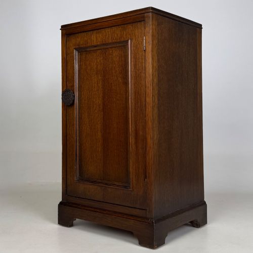 fig 2. A standing antique dark oak bedside cabinet with a single framed door, a round carved handle, and a solid plinth base.