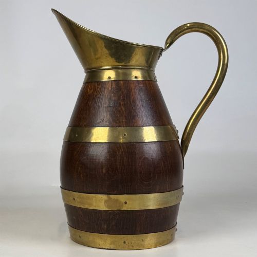fig 1. A tall dark oak wooden jug styled as an umbrella stand, featuring decorative brass bands, a curved brass handle, and a brass spout.