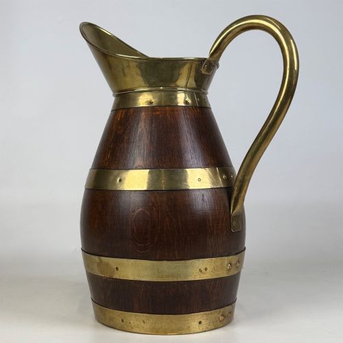 fig 2. A tall dark oak wooden jug styled as an umbrella stand, featuring decorative brass bands, a curved brass handle, and a brass spout.