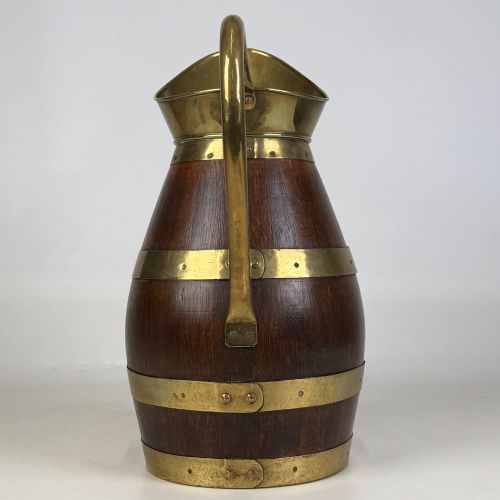 fig 3. A tall dark oak wooden jug styled as an umbrella stand, featuring decorative brass bands, a curved brass handle, and a brass spout.