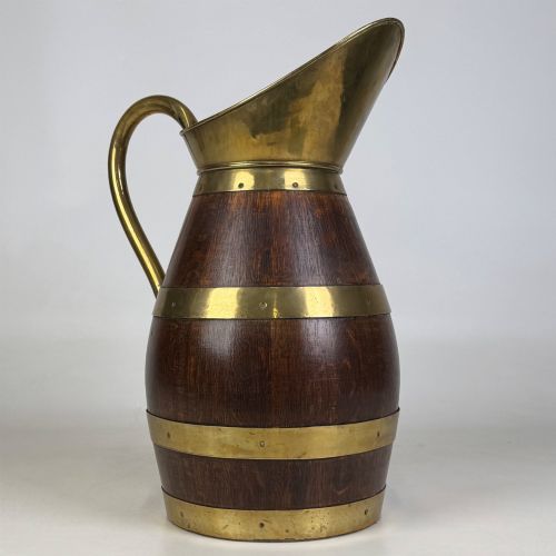 fig 6. A tall dark oak wooden jug styled as an umbrella stand, featuring decorative brass bands, a curved brass handle, and a brass spout.