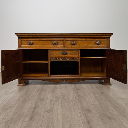 fig 1. An early 20th-century oak Arts and Crafts sideboard featuring hand-carved foliate panels, copper drop handles, multiple drawers, and a central open recess.