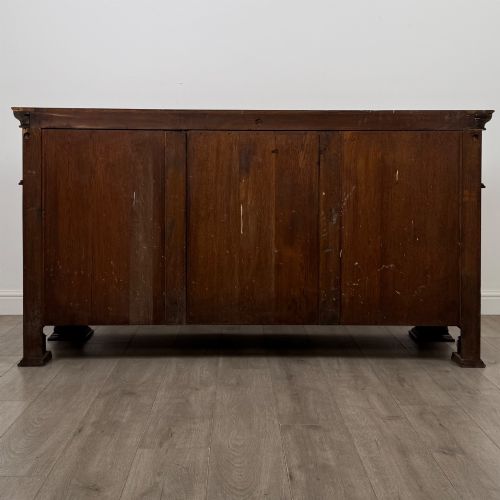 fig 5. An early 20th-century oak Arts and Crafts sideboard featuring hand-carved foliate panels, copper drop handles, multiple drawers, and a central open recess.