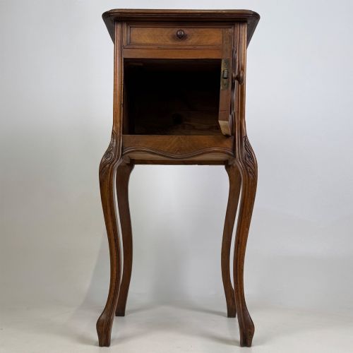 fig 1. An antique French walnut bedside cabinet featuring high slender cabriole legs, a single drawer, and a carved wooden door with a marquetry panel.