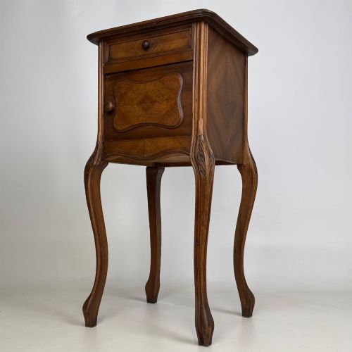 fig 2. An antique French walnut bedside cabinet featuring high slender cabriole legs, a single drawer, and a carved wooden door with a marquetry panel.