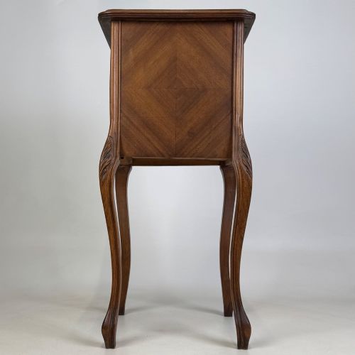 fig 3. An antique French walnut bedside cabinet featuring high slender cabriole legs, a single drawer, and a carved wooden door with a marquetry panel.