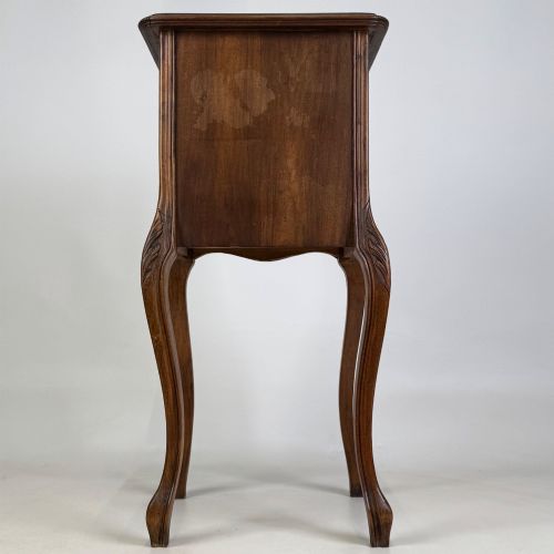 fig 5. An antique French walnut bedside cabinet featuring high slender cabriole legs, a single drawer, and a carved wooden door with a marquetry panel.