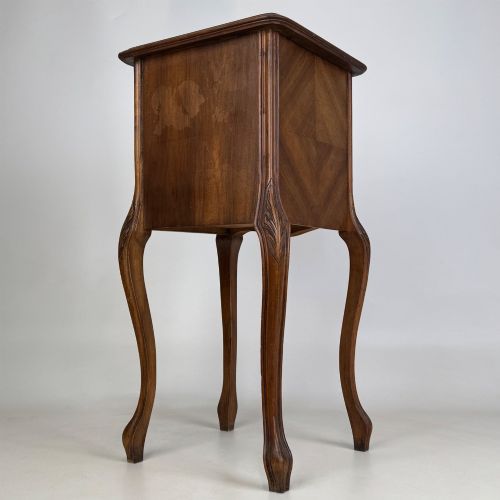 fig 6. An antique French walnut bedside cabinet featuring high slender cabriole legs, a single drawer, and a carved wooden door with a marquetry panel.