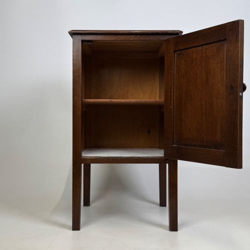 fig 1. An Edwardian dark brown oak cabinet featuring a single panelled door with a round wooden knob supported on four square straight legs.