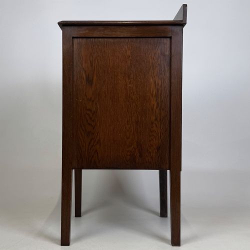 fig 3. An Edwardian dark brown oak cabinet featuring a single panelled door with a round wooden knob supported on four square straight legs.