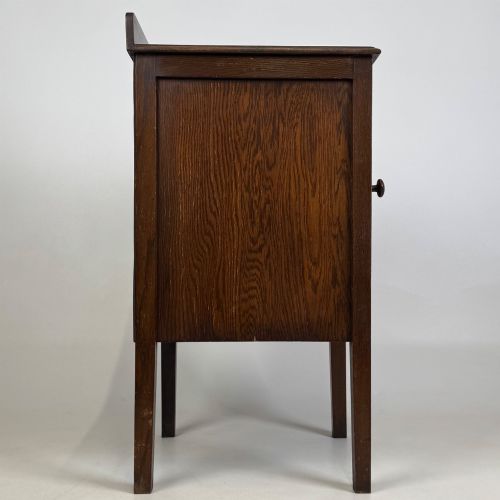 fig 7. An Edwardian dark brown oak cabinet featuring a single panelled door with a round wooden knob supported on four square straight legs.