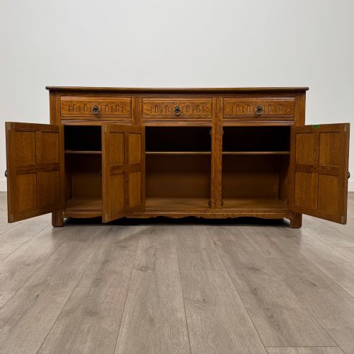 fig 1. A three-door golden oak sideboard featuring three carved drawers, panelled cabinet doors, and metal drop handles.