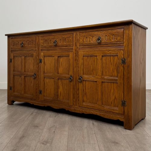 fig 2. A three-door golden oak sideboard featuring three carved drawers, panelled cabinet doors, and metal drop handles.