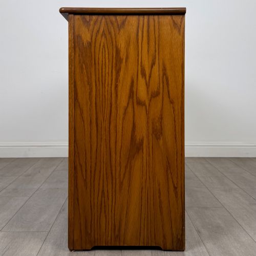 fig 3. A three-door golden oak sideboard featuring three carved drawers, panelled cabinet doors, and metal drop handles.