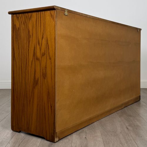 fig 4. A three-door golden oak sideboard featuring three carved drawers, panelled cabinet doors, and metal drop handles.