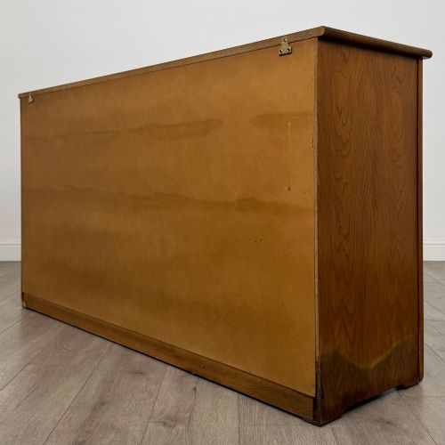 fig 6. A three-door golden oak sideboard featuring three carved drawers, panelled cabinet doors, and metal drop handles.