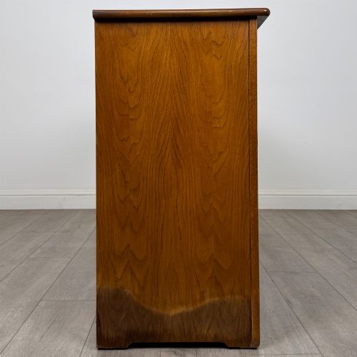 fig 7. A three-door golden oak sideboard featuring three carved drawers, panelled cabinet doors, and metal drop handles.