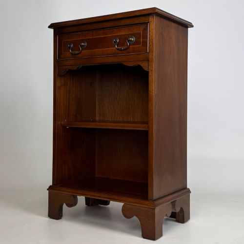fig 1. A small mahogany open bookcase featuring a single top drawer with brass swan-neck handles, satinwood inlay, open lower shelving, and shaped bracket feet.