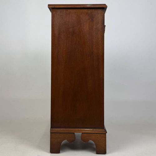 fig 6. A small mahogany open bookcase featuring a single top drawer with brass swan-neck handles, satinwood inlay, open lower shelving, and shaped bracket feet.