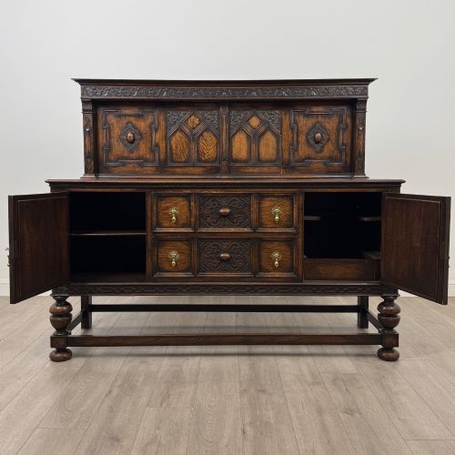 fig 1. A dark oak Jacobean style sideboard featuring a raised upper superstructure, geometric carved panelling, drawers with brass drop handles, and turned bulbous legs connected by a stretcher base.