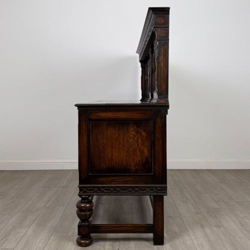 fig 3. A dark oak Jacobean style sideboard featuring a raised upper superstructure, geometric carved panelling, drawers with brass drop handles, and turned bulbous legs connected by a stretcher base.
