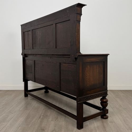 fig 6. A dark oak Jacobean style sideboard featuring a raised upper superstructure, geometric carved panelling, drawers with brass drop handles, and turned bulbous legs connected by a stretcher base.