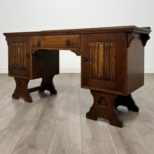 fig 2. A 20th-century carved oak pedestal desk featuring linenfold cupboard doors, a central top drawer, and trefoil pierced end supports.