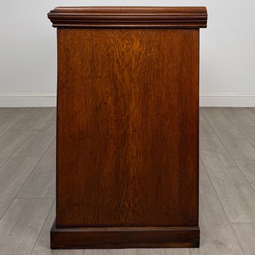 fig 3. A wide 19th-century Victorian dark oak sideboard featuring relief-carved floral panels, central drawers with brass handles, and lower cupboard doors.