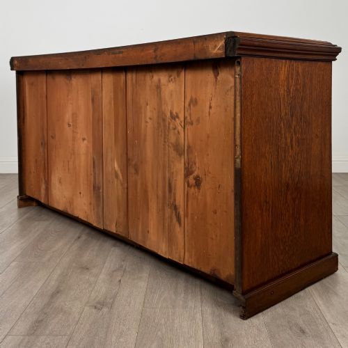 fig 6. A wide 19th-century Victorian dark oak sideboard featuring relief-carved floral panels, central drawers with brass handles, and lower cupboard doors.
