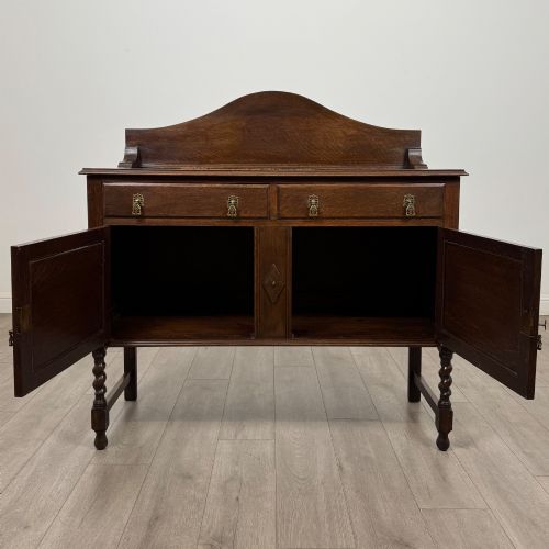 fig 1. An Edwardian dark oak sideboard featuring a shaped upstand gallery, two top drawers with brass drop handles, twin raised-panel cupboard doors, and front barley twist legs.